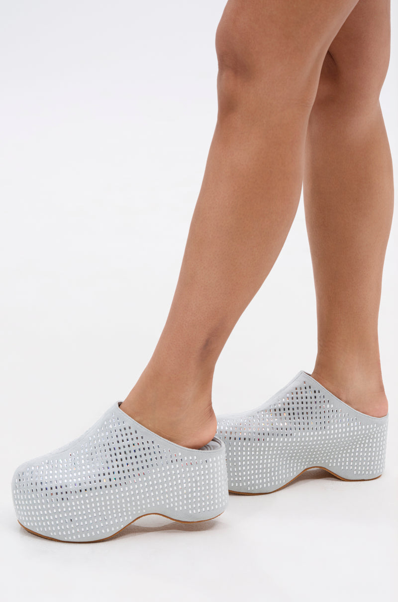 Standing on tiptoe, only lower legs and feet are seen wearing the AZALEA WANG ROMESCO BLING FLATFORM CLOG IN GREY, featuring small white perforated dots, set against a plain white background.
