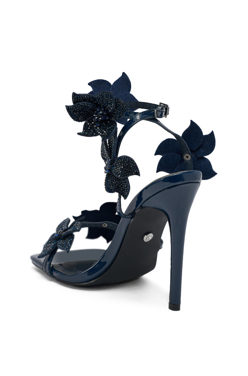 The AZALEA WANG ROMI Rhinestone Embellished Navy Dressy Sandal features a stiletto heel and textured floral appliqués, shown from the rear against a white background.