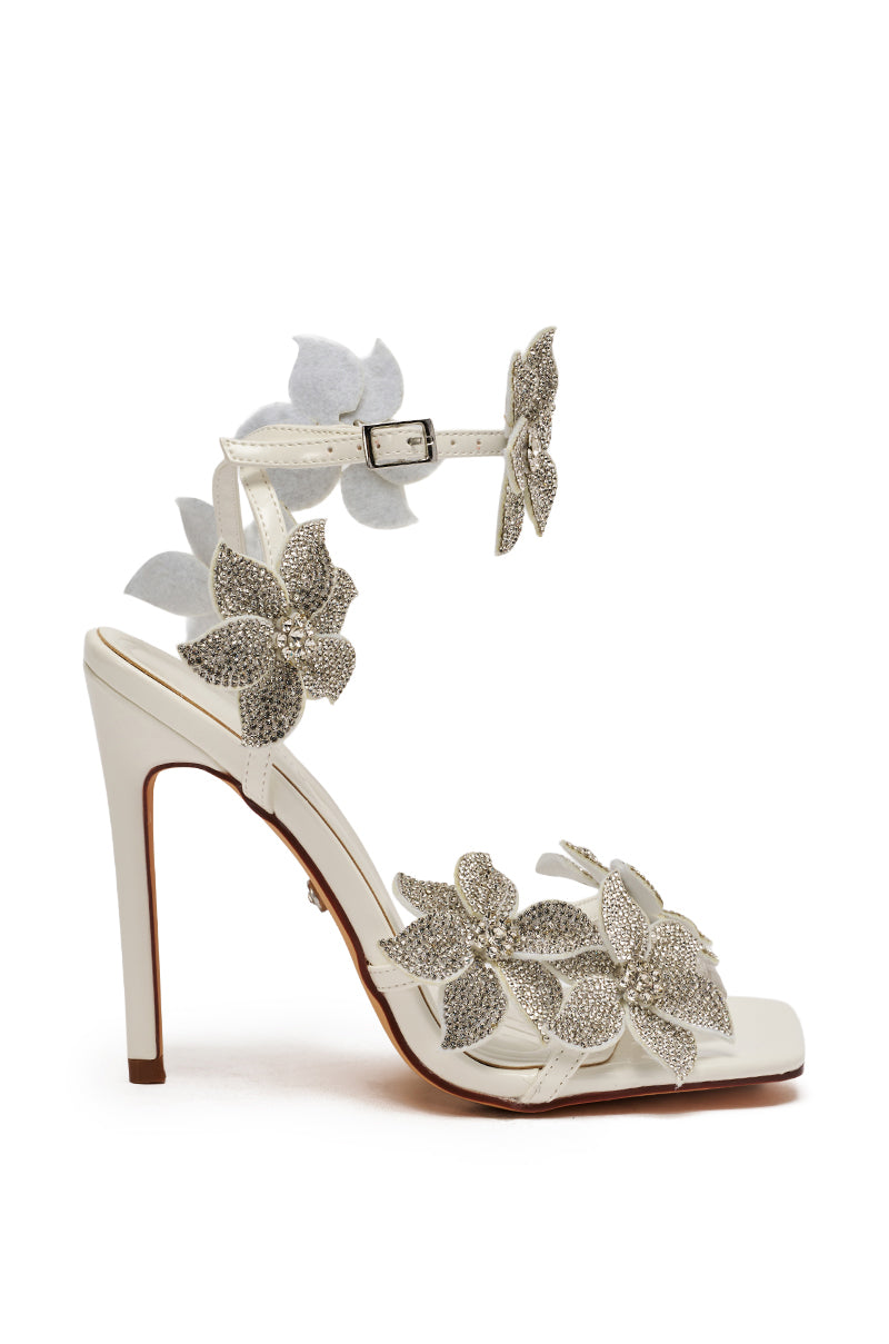 The AZALEA WANG ROMI White Floral With Rhinestones Stiletto Sandal features a faux leather high heel, open toe, thin ankle strap, and sparkling silver rhinestone flower accents on the front, side, and ankle strap.