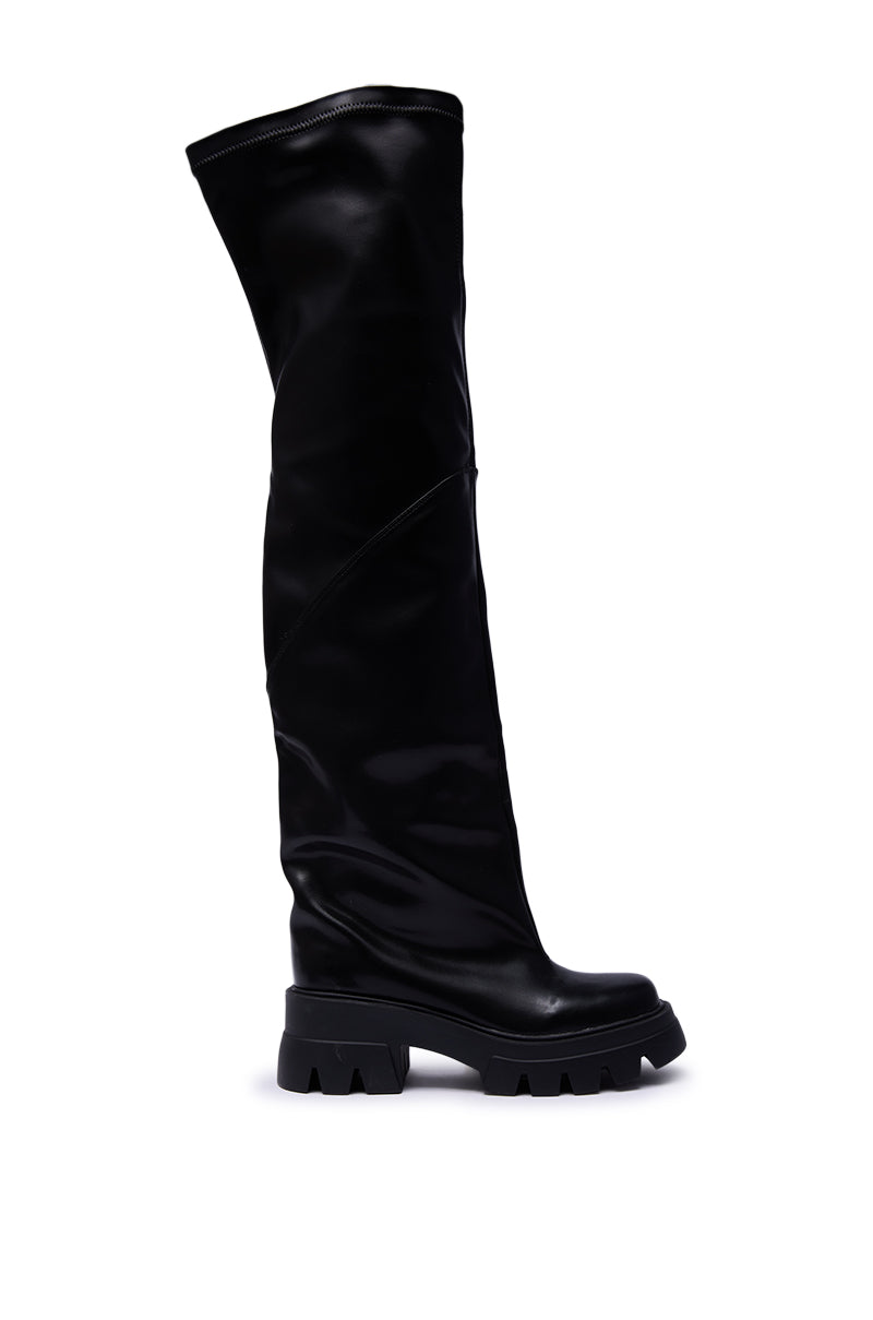 The AZALEA WANG RONAN BLACK SLOUCH BOOT is a black, knee-high faux leather boot with a chunky treaded sole and a smooth, slightly shiny finish, shown in a side view against a white background.