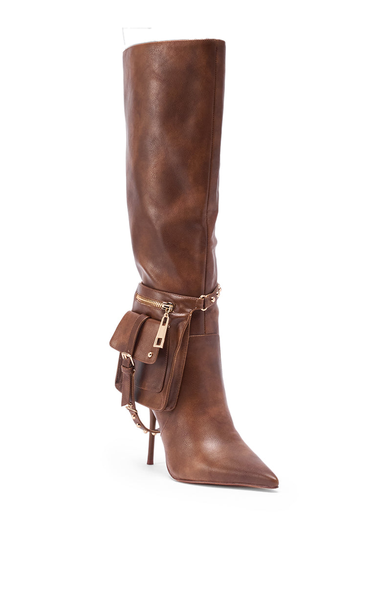 The AZALEA WANG RONDEL BROWN DISTRESSED STILETTO BOOT is a tall, brown leather boot with a pointed toe, a small pouch with gold zipper and lock, plus a thin chain accent around the ankle.