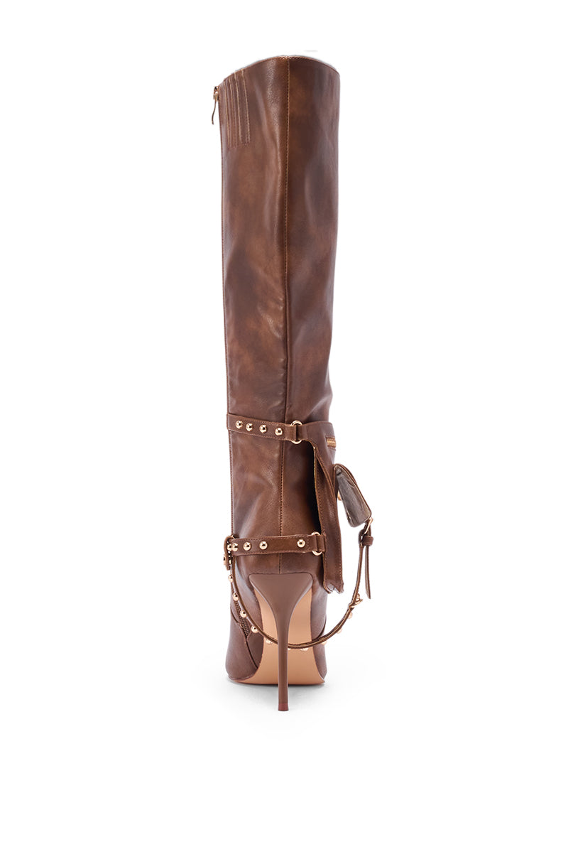 The AZALEA WANG RONDEL BROWN DISTRESSED STILETTO BOOT is a tall brown leather boot with a pointed toe, slim stiletto heel, metal studs, and decorative straps wrapped around the ankle and shaft, shown from the back.