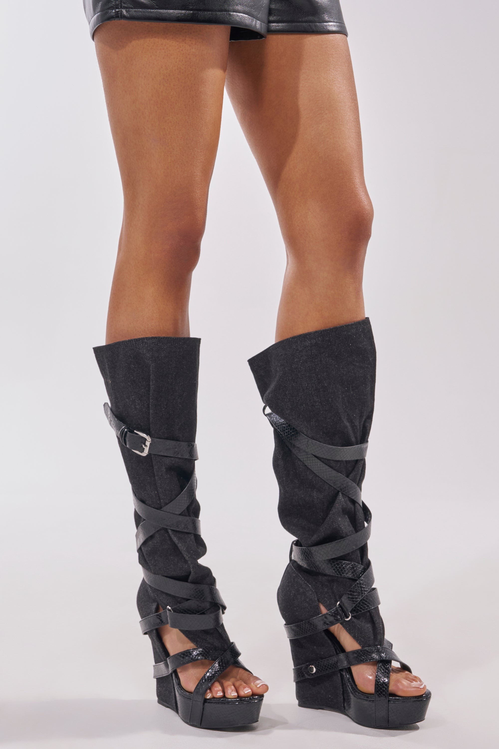 Wearing the AZALEA WANG ROTHKID BLACK DENIM KNEE HIGH OPEN TOE BOOT, this person stands against a plain background, channeling the bold edge of statement streetwear with black denim knee-high open-toe boots. 2