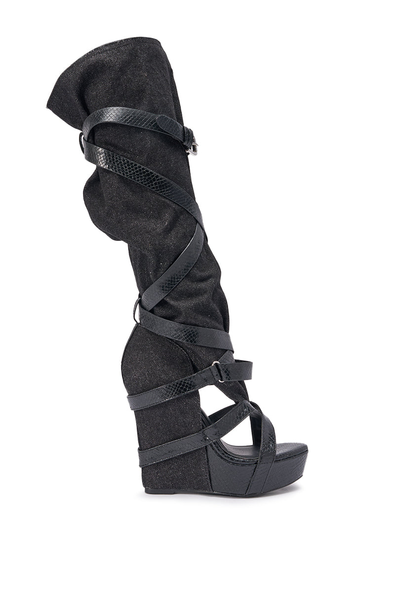 The AZALEA WANG ROTHKID Black Denim Knee High Open Toe Boot features a black wedge heel, multiple crisscrossing straps, and a textured finish, shown from the side on a white background. 1