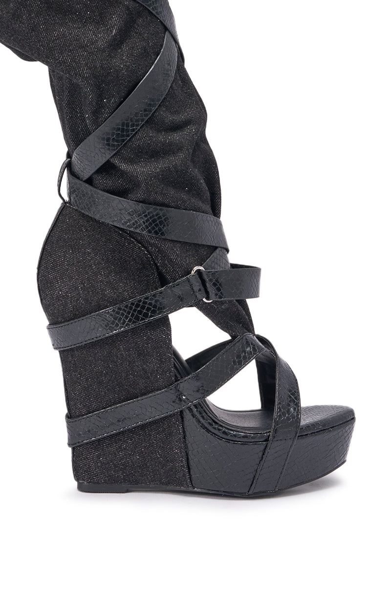 A close-up of the AZALEA WANG ROTHKID BLACK DENIM KNEE HIGH OPEN TOE BOOT, featuring a black denim finish and crisscrossing straps, styled with black denim pants. 6