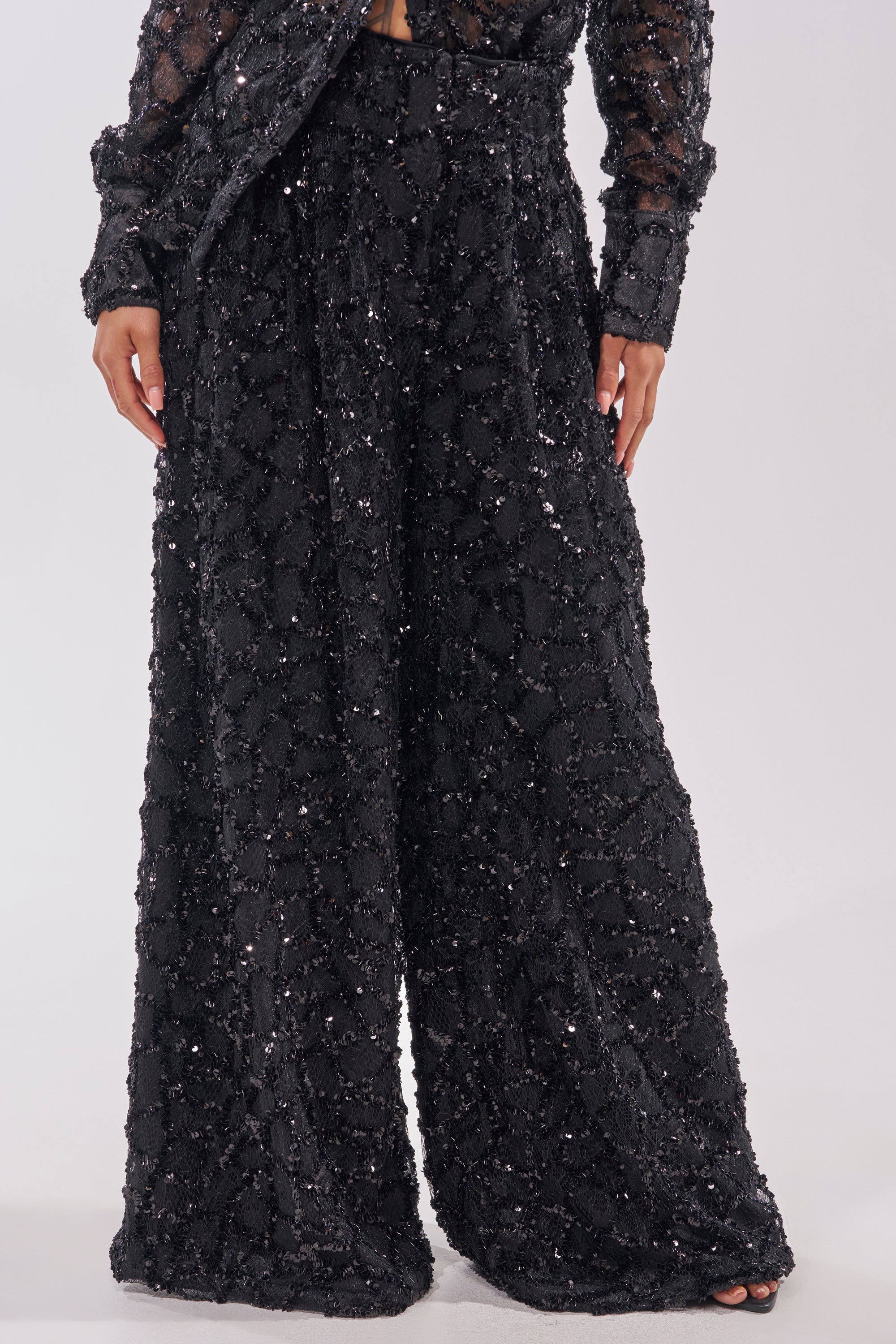 Someone wearing the ROXY SEQUIN PALAZZO PANT—elegant, high-waisted, wide-leg trousers adorned with black sequins—paired with a matching long-sleeve top for a sparkly and sophisticated look. 2