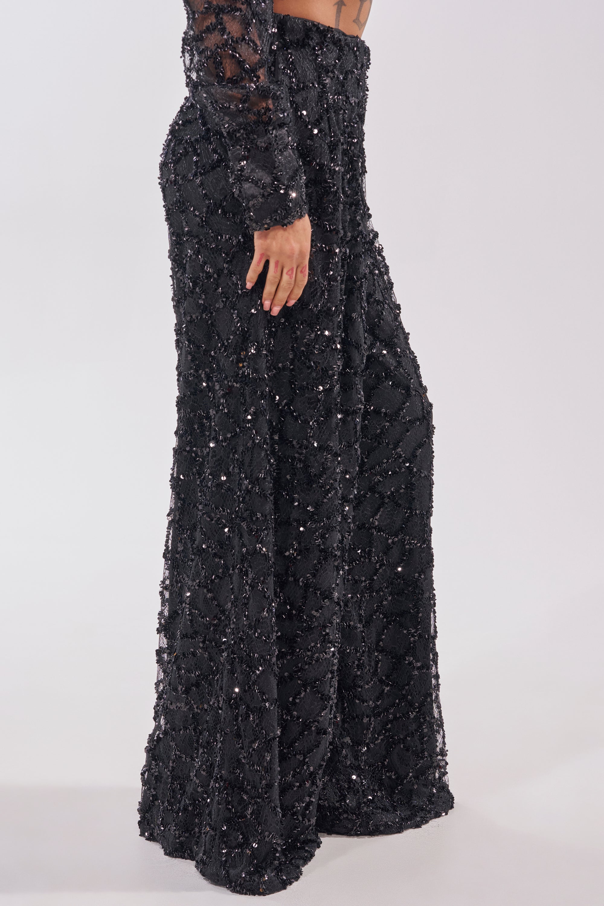 A person wears the ROXY SEQUIN PALAZZO PANT, featuring a high waist and wide-leg silhouette, with a matching long-sleeve top with sheer accents, posed against a plain white background. 4