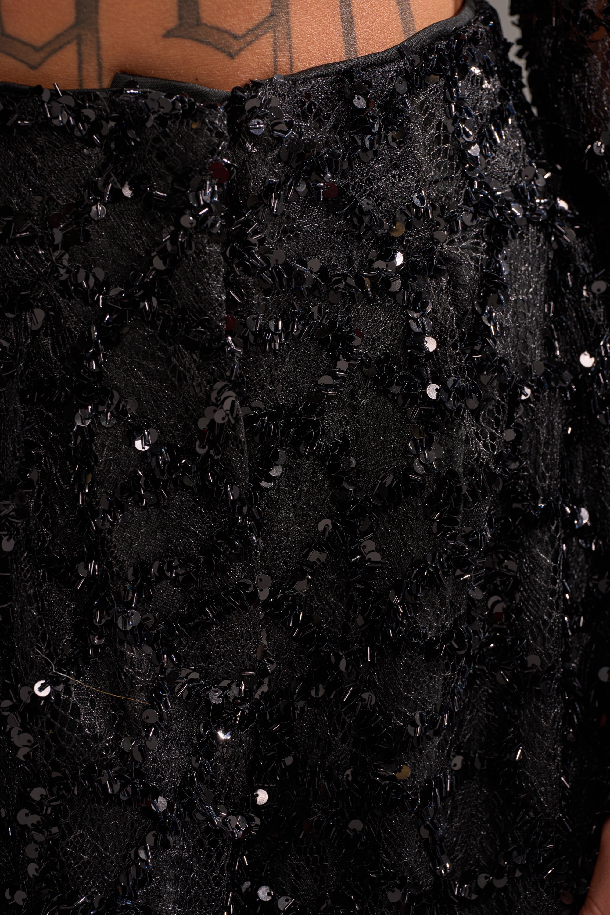 Close-up of the ROXY SEQUIN PALAZZO PANT in black, featuring textured lace fabric and shimmering sequins, with a glimpse of tattooed skin at the top edge.