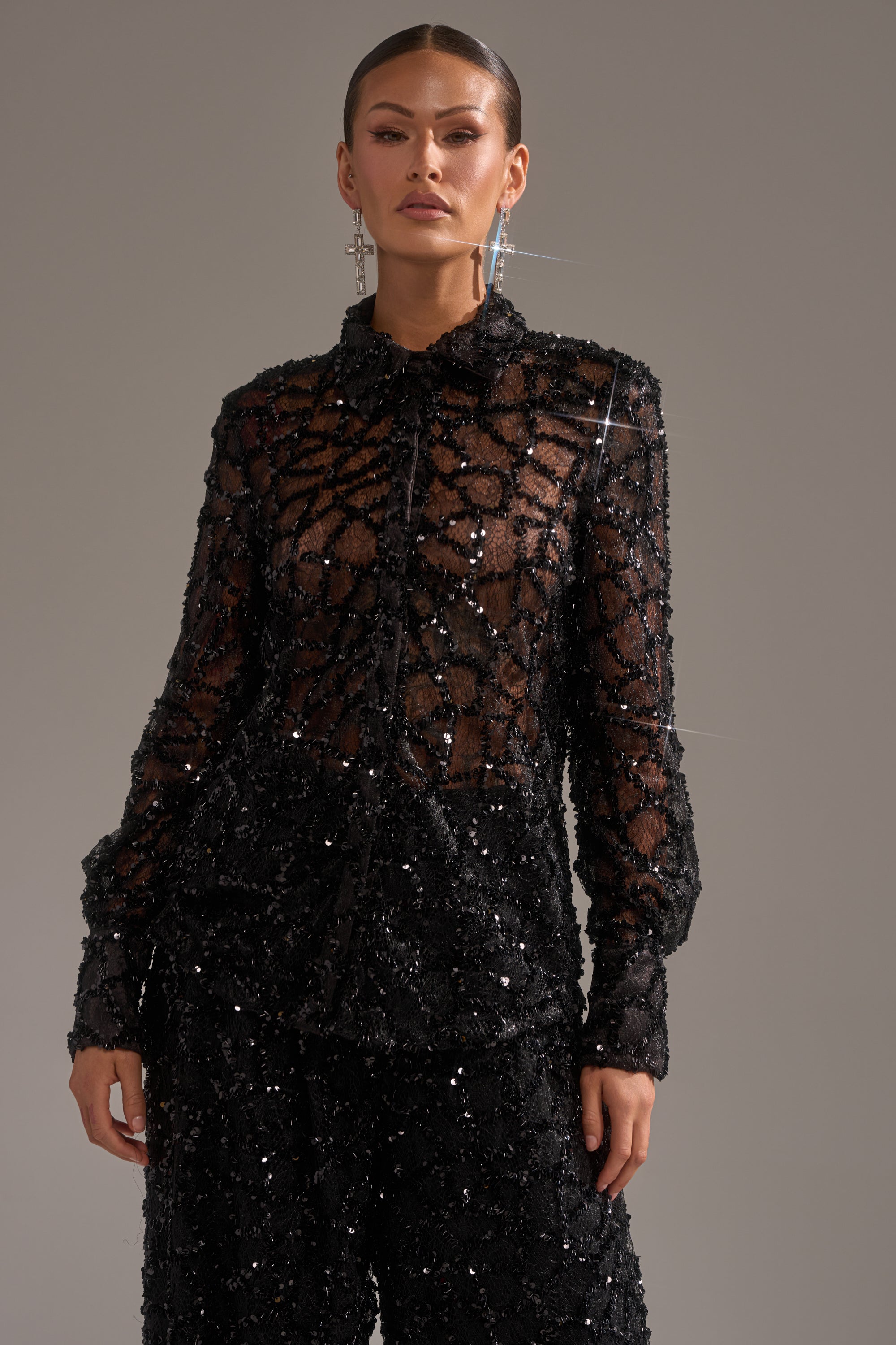 A person stands against a plain background in the ROXY SEQUIN BUTTON DOWN and matching sequin pants, creating an elevated evening look with slicked-back hair and statement earrings.