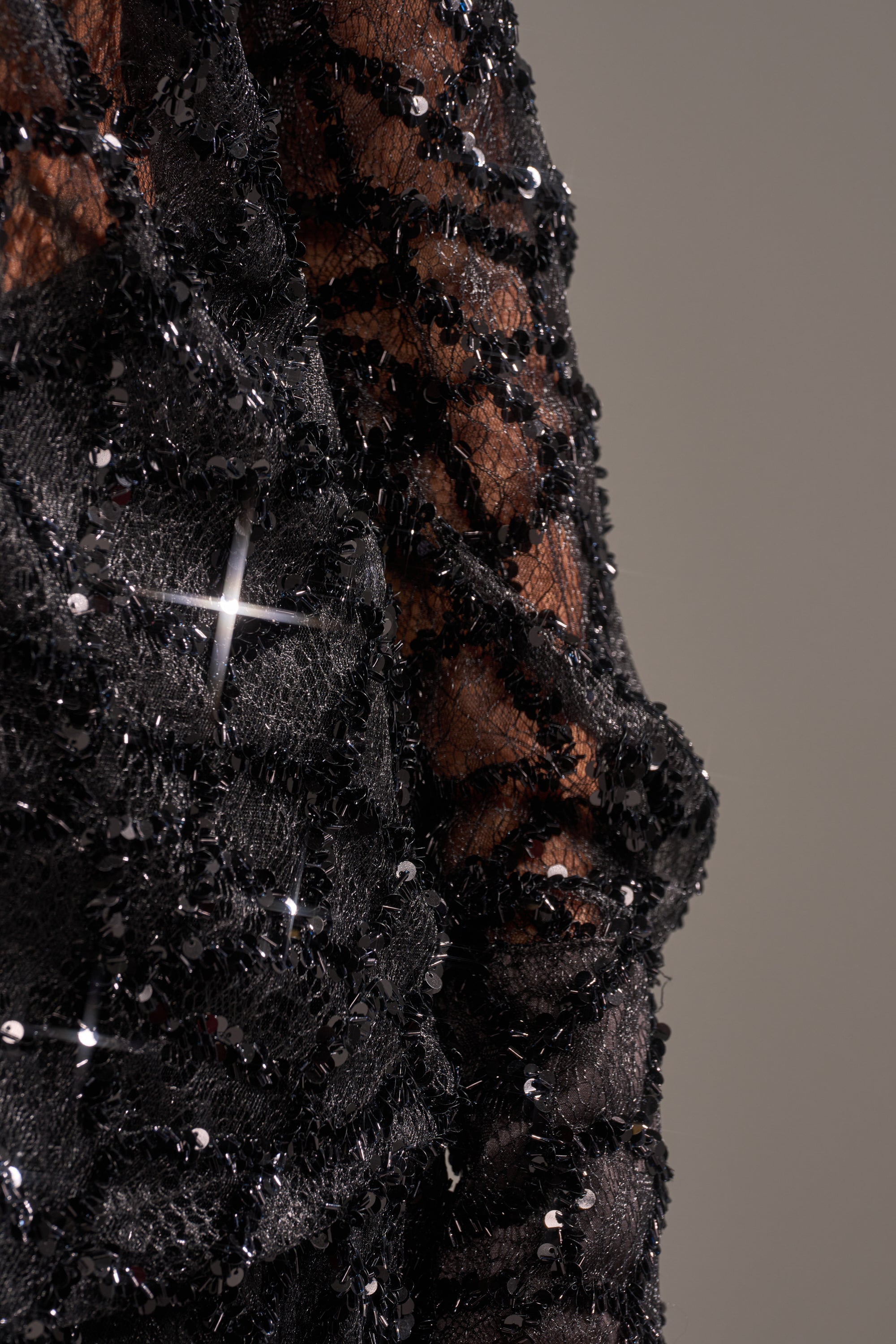 Close-up of the ROXY SEQUIN BUTTON DOWN’s black mesh fabric with intricate beading and sequins, perfect for a sheer blouse that adds sparkle to any evening look. The neutral background highlights its delicate, glittering details.