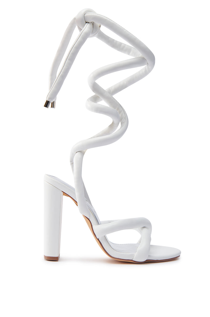 The ROYALE WHITE PU PUFF CHUNKY LACE UP SANDAL boasts a modern twist with its open toe design and unique spiral ankle strap. The faux leather upper intricately wraps around the leg, while the chunky rectangular heel adds an elevated, stylish appearance. 2