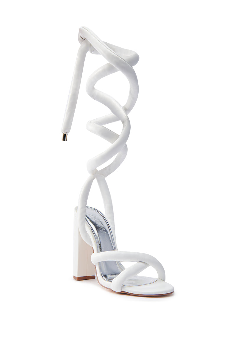 The ROYALE WHITE PU PUFF CHUNKY LACE UP SANDAL features a faux leather upper, cushioned strap that spirals artistically around the ankle, an open almond toe, and a sturdy heel, combining elegance and comfort on a plain white background. 3