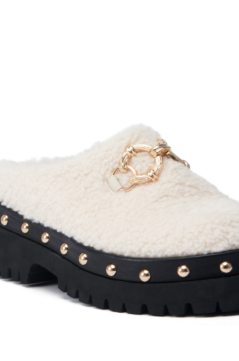 The AZALEA WANG ROZELE BEIGE CLOG is a cozy, slip-on shoe with a chunky black platform lug sole. It showcases a faux sherpa design, adorned with gold studs along the edge of the sole and features an elegant gold chain detail on top.