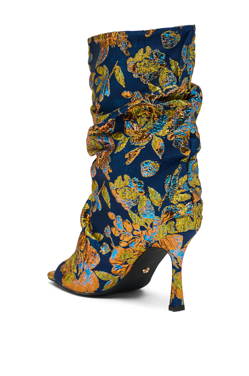 The AZALEA ROZSI Blue Multi Brocade Open Toe Stiletto Bootie features vibrant blue metallic brocade with gold, green, and orange florals, a pointed toe, slouchy ruched design, open toe, and slender stiletto heel.