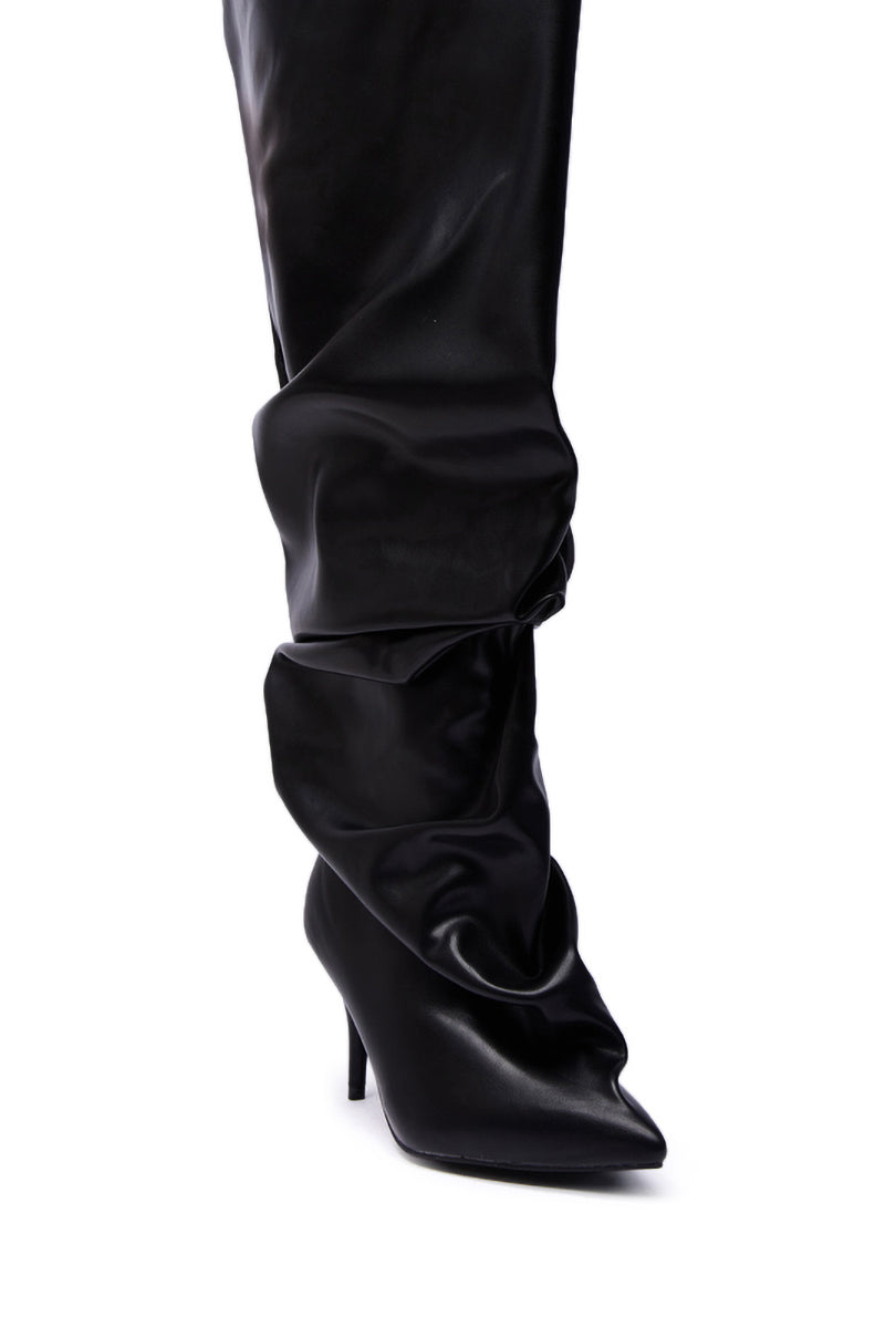 A close-up of the AZALEA WANG RUBIUS BLACK EXTREME RUCHED BOOT—a black, slouchy knee-high with a pointed toe and high heel, crafted from shiny faux leather.