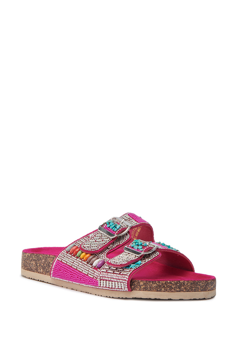 The AKIRA RUVY FUCHSIA STONE EMBELLISHED FLAT SANDAL is a vibrant slip-on with a cork sole, rhinestone details, two buckle straps, pink and turquoise accents, and a soft velvet footbed.