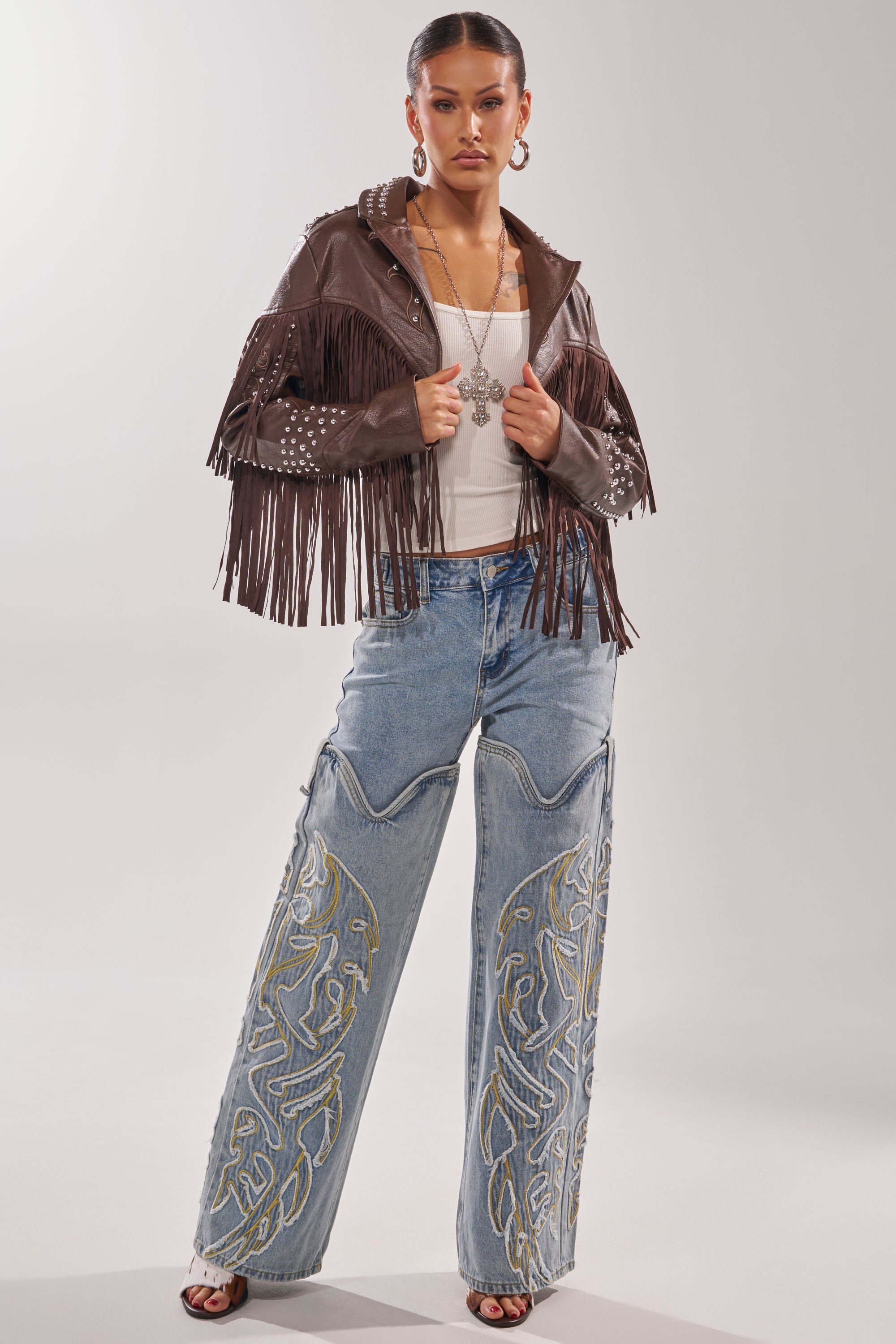 A woman poses in the NOT MY FIRST RODEO CROPPED MOTO jacket, a white top, and wide-leg embroidered blue jeans. She completes the look with hoop earrings, a statement chain necklace, and open-toed shoes. 8