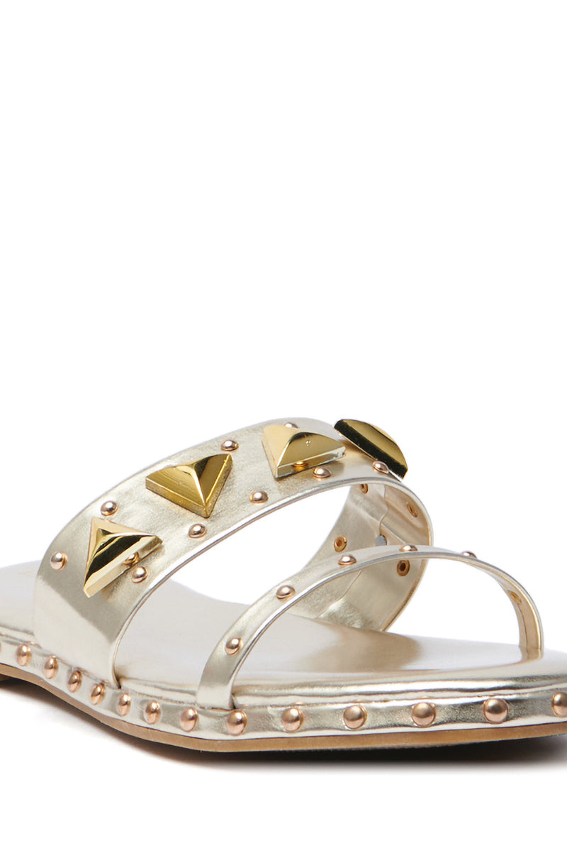 The AKIRA RYLIE GOLD EMBELLISHED SLIP ON SANDAL features metallic faux leather, two straps with gold pyramid and round studs, an open-toe design, and a chunky heel for an elegant touch.