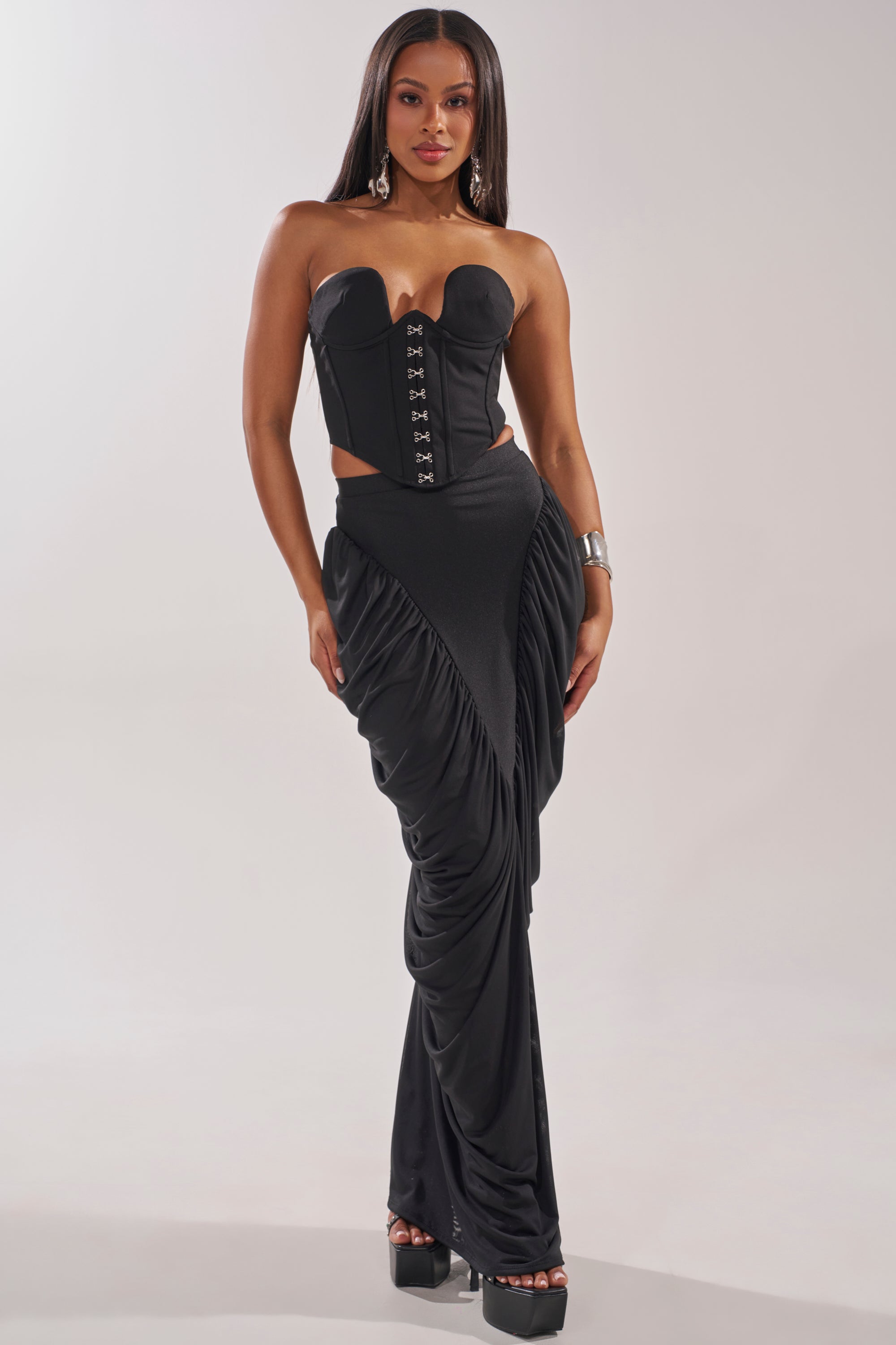 A woman exudes confidence in a strapless black corset top and the DREAMY RUCHED SKIRT featuring a high-rise waistband. She styles her long, straight hair with a chunky metallic cuff and elevated platform heels. 5