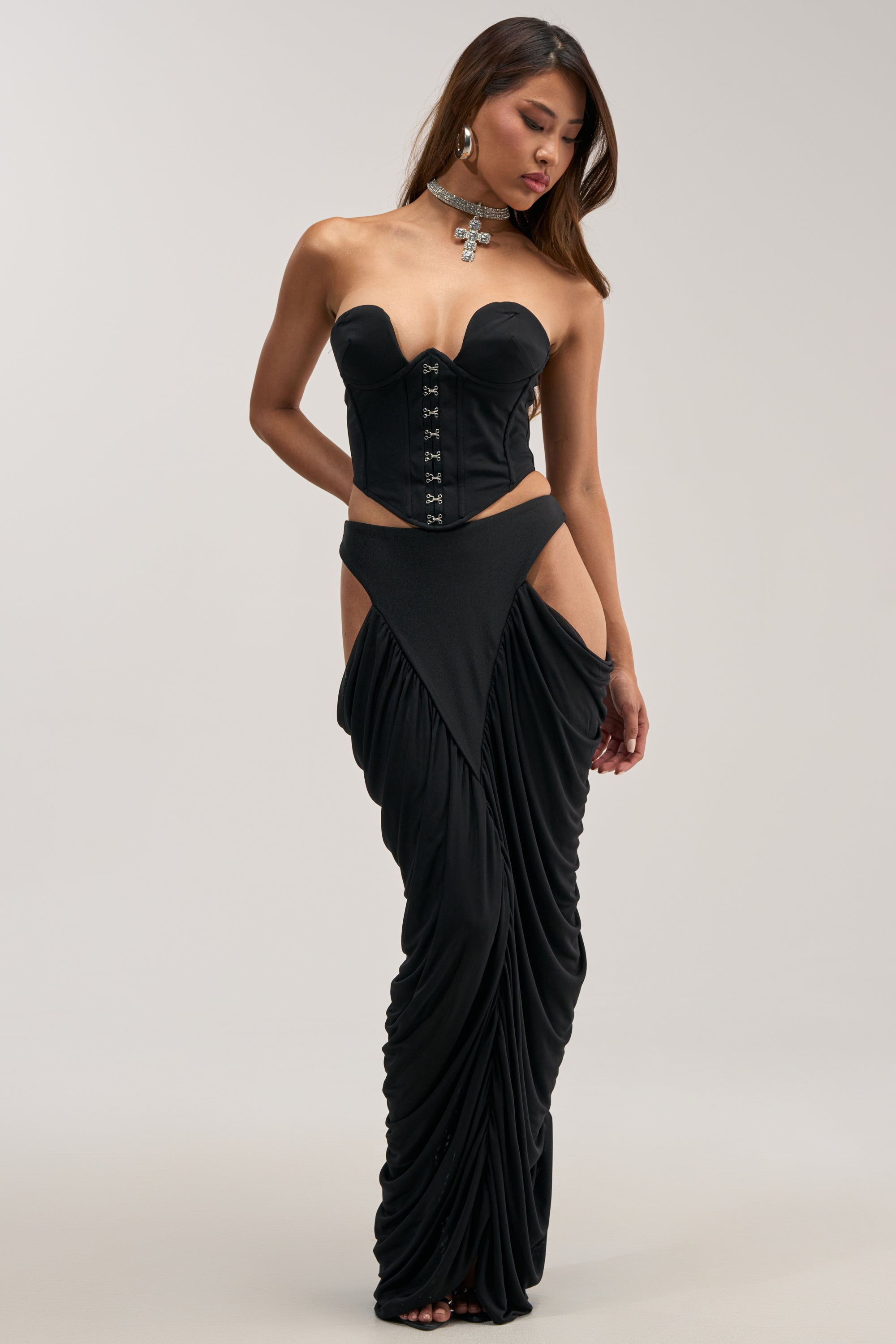 A woman poses against a plain background wearing a strapless black corset with hook closures, paired with the HOTTIE ALERT MESH MAXI SKIRT featuring dramatic high waist and bold hip cutouts.