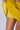 A person lifts the hem of their DONT LOOK BACK VELVET MINI SKIRT, revealing yellow shorts underneath. The image also partially shows a tattoo on their side. The background is a plain light grey.