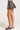 A person wearing the "Out of Our Head Wool Mini Skirt in Grey," an ideal addition to any fall wardrobe, paired with black pointed-toe mules with a low heel, stands elegantly against a light background.