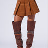 A person wearing the "RUN AFTER YOU CORDUROY MINI SKIRT IN BROWN," paired with brown, knee-high open-toe boots adorned with decorative studs. The top part of the ensemble includes a white garment with brown accents visible above the skirt. This chic look is enhanced by built-in shorts for added comfort, all set against a plain white background.