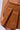 A close-up shot features a person wearing the RUN AFTER YOU CORDUROY MINI SKIRT IN BROWN. The high-rise silhouette, along with the pleats and texture of the skirt, are clearly visible. The person's hand rests against their hip, highlighting the midsection against a plain background.