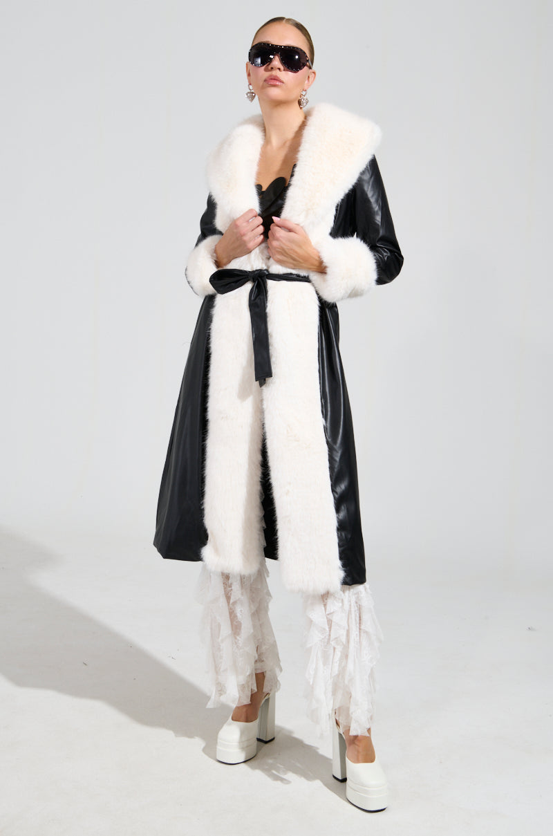 Dressed in the CANT GET ENOUGH FUR TRENCH with striking white trim, accessorized with large sunglasses, layered white lace pants, and white platform heels, an individual stands confidently against a plain background.