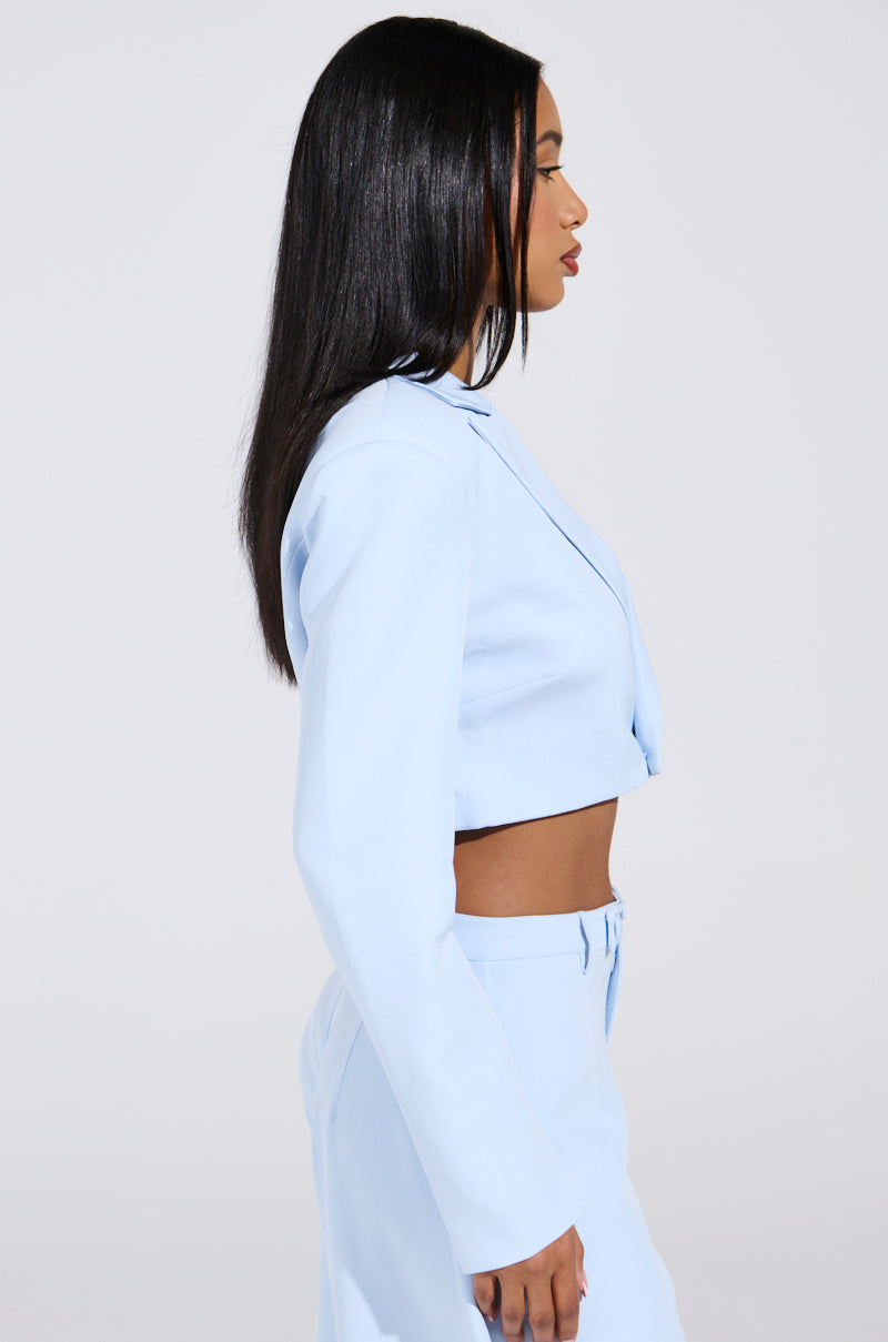 A person with long black hair is seen from the side, styled in a LOTTIE Cropped Blazer in light blue, paired with matching high-waisted pants against a plain, light-colored background.
