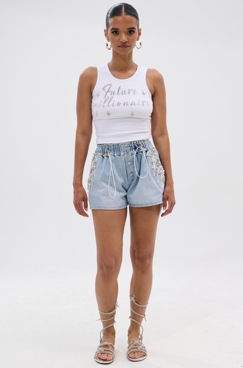 A woman faces forward in a white "Future Millionaire" tank top, BLING BLING PEARL DENIM SHORTS with beaded fringe, and lace-up sandals against a plain white background. 6