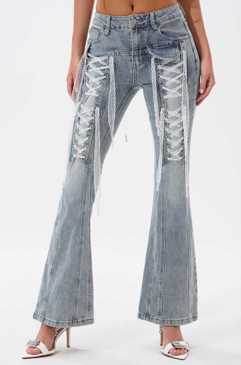 A person wears TIED UP FLARE JEANS featuring white lace-up detailing on the front thighs and knees, paired with open-toe high-heeled shoes. The photo is cropped at the torso. 0