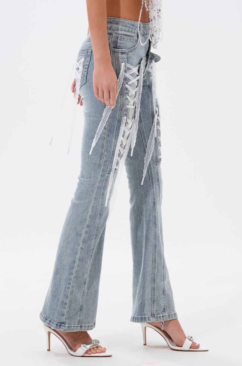A person wearing TIED UP FLARE JEANS with white lace-up side details and white high-heeled sandals stands against a plain white background. 2