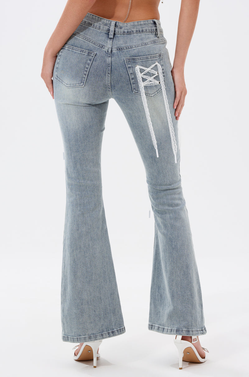 A person models the TIED UP FLARE JEANS, light blue denim flares with white lace-up detail on the back pocket, seen from behind and styled with white high-heeled sandals. 3