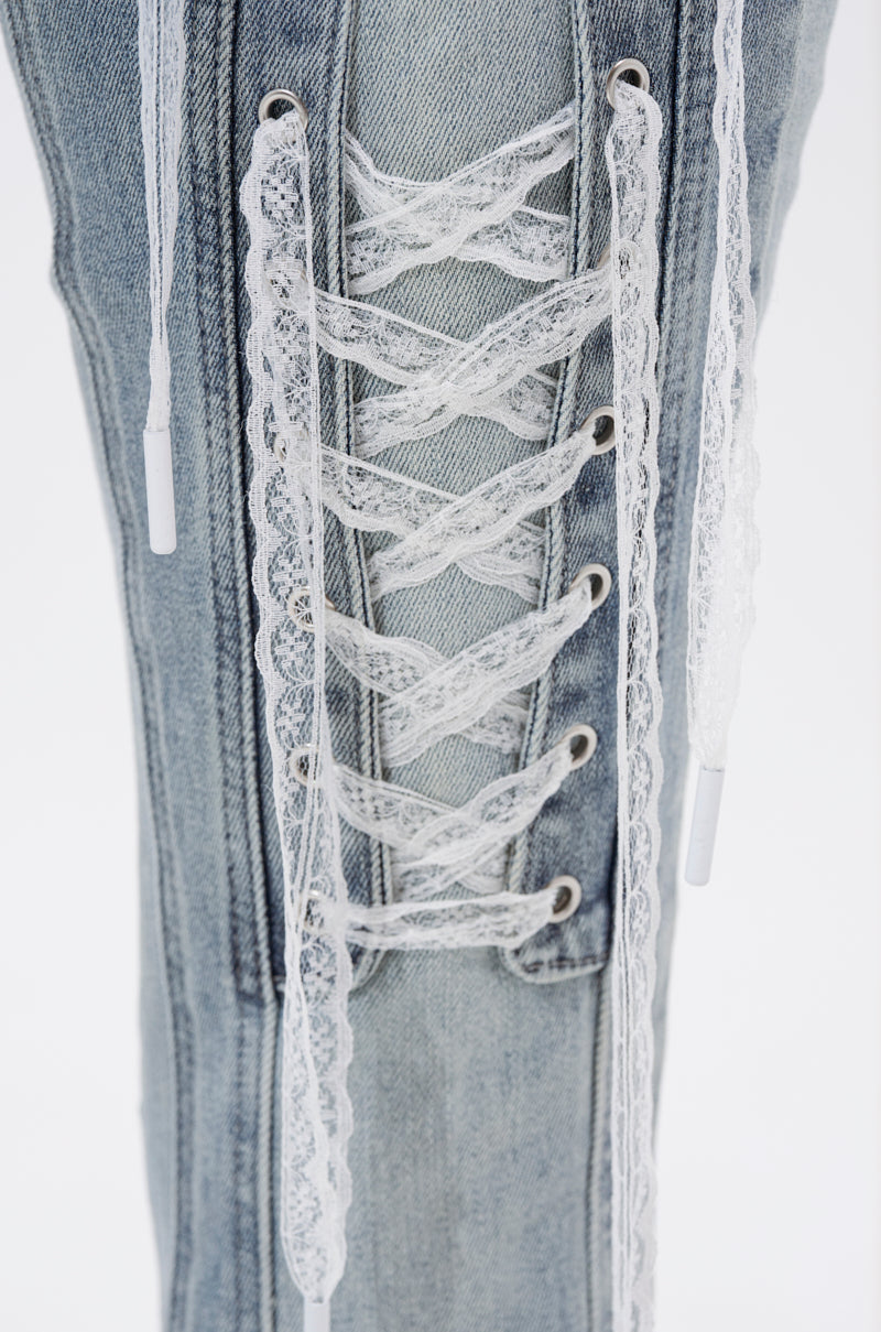 Close-up of the TIED UP FLARE JEANS in light-wash denim, featuring a vertical lace-up detail with white, lace-textured shoelaces threaded through metal eyelets along the leg. 6