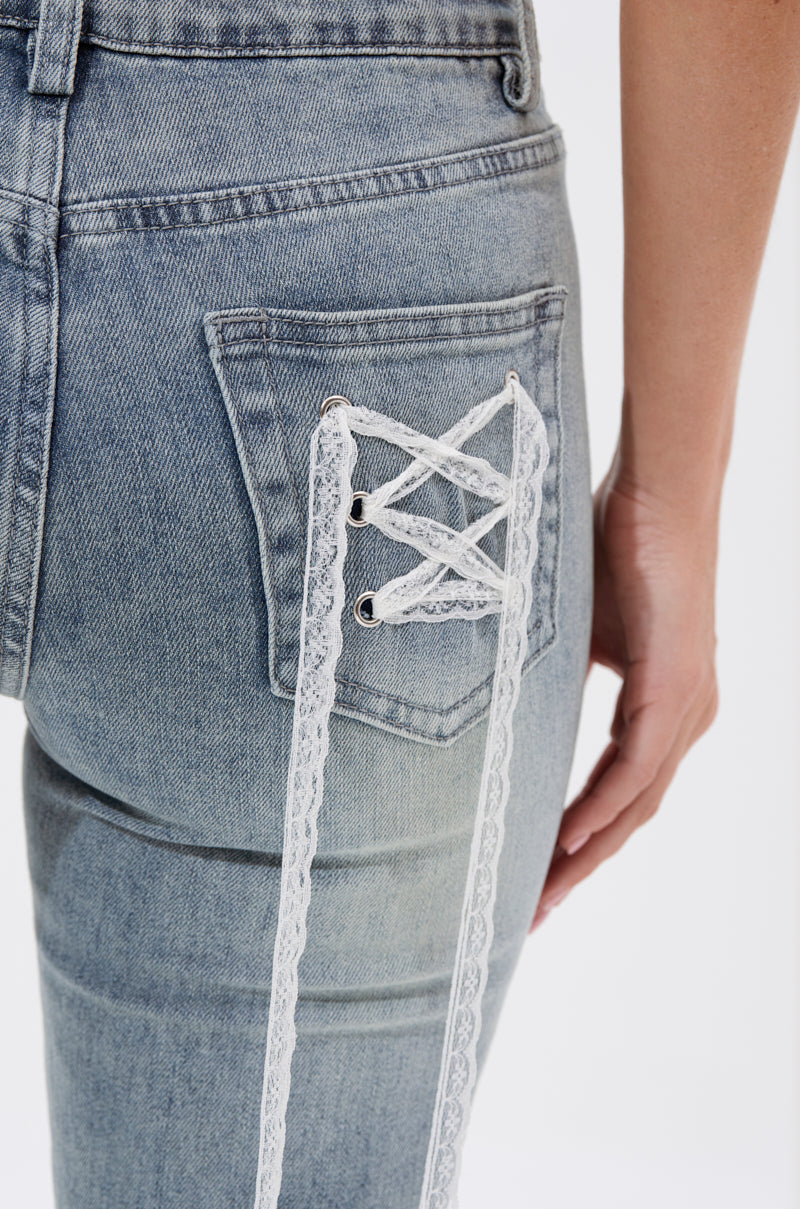 A close-up of someone wearing the TIED UP FLARE JEANS—light-wash, lace-up denim with a back pocket featuring white lace threaded through eyelets in a corset-like crisscross pattern. One hand rests by their side. 7