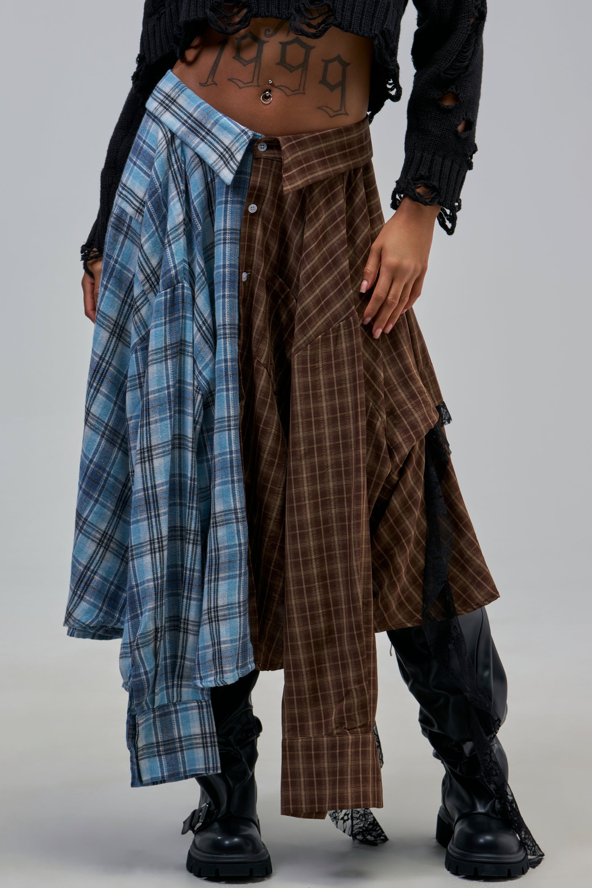 A person wearing the FEELING ALL THE VIBES PLAID SKIRT paired with a black cropped sweater and black boots, shown from shoulders down.