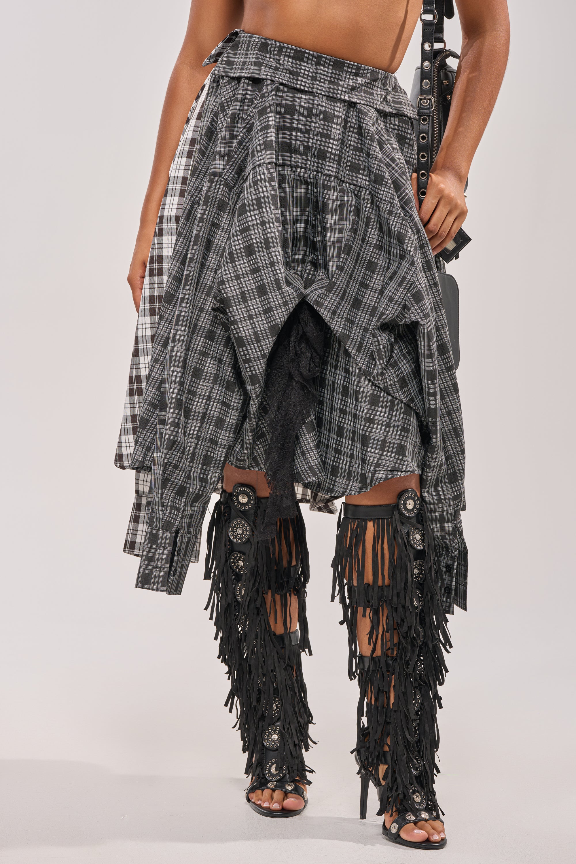Wearing the FALL VIBES PLAID MIDI SKIRT, a person pairs it with black fringed knee-high open-toe boots featuring decorative details, striking a pose with one hand on their hip. 3