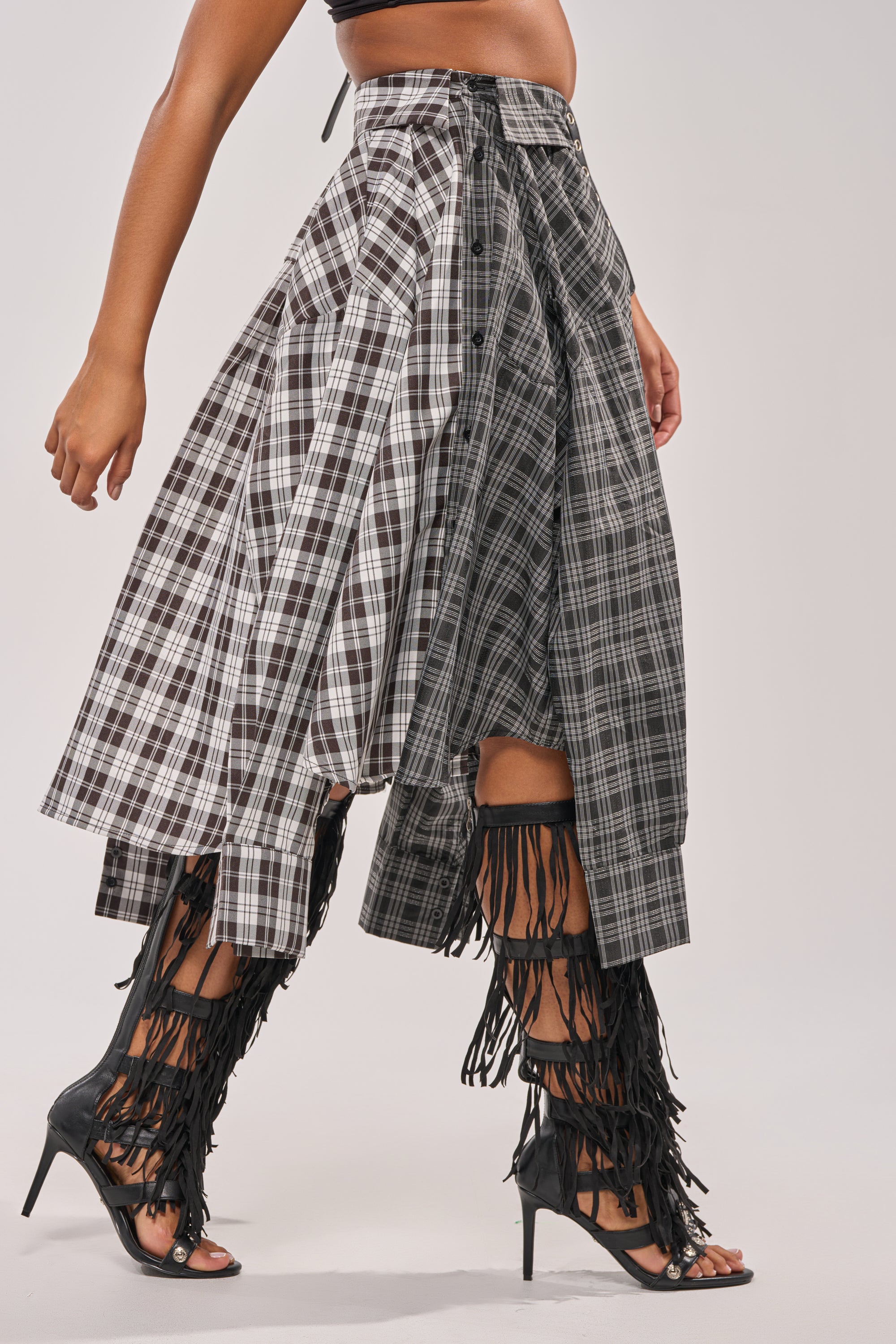 Only the lower body is visible, wearing the FALL VIBES PLAID MIDI SKIRT with an asymmetrical hem and layered panels, paired with black fringe high-heeled sandals—a chic festival statement look. 7