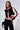 A woman stands confidently wearing a sporty black RAYE Cropped Bomber with red and white striped sleeves, paired with matching high-waisted pants. The sleek knit fabrication complements her long, straight hair and hoop earrings as she poses against a plain white background.