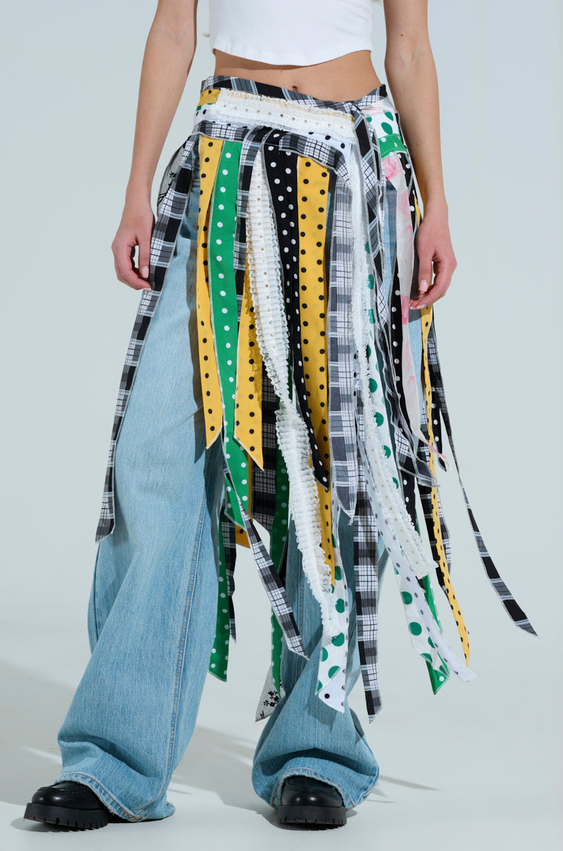 Someone in a white crop top and blue wide-leg jeans featuring multicolored, patterned ribbons—stripes, polka dots, and checks—from the "Oh So Chic Pattern Mix Belt Skirt" line pairs the look with black chunky shoes against a plain background.