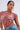 A person wearing the BEJEWELED RUBY SLEEVELESS TOP, designed with interlinked red and silver pieces resembling gemstones, pairs it with large hoop earrings and stylish blue jeans against a simple light gray background.