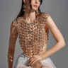 A woman with long brown hair poses in the BEJEWELED GOLD SLEEVELESS TOP, its sparkling gemstone embellishments catching the light. She pairs it with a white tulle skirt and large earrings, gazing to the side against a neutral background.