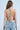 A woman with long brown hair faces away from the camera, wearing the BLING BLING TOP. The backless halter top features sequin discs and multiple thin straps, paired effortlessly with light blue jeans against a plain light blue background.