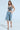 A woman confidently poses against a plain background, showcasing the BLING BLING TOP with sequin discs and faded denim shorts featuring distressed details. Her party-perfect look is completed with long wavy hair and heeled sandals.