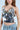 A woman in the silver BLING BLING TOP adorned with iridescent sequins stands against a light blue background. Her long, wavy hair cascades over light-wash denim jeans as she slightly tilts her head, exuding a party-ready vibe with one hand on her hip.