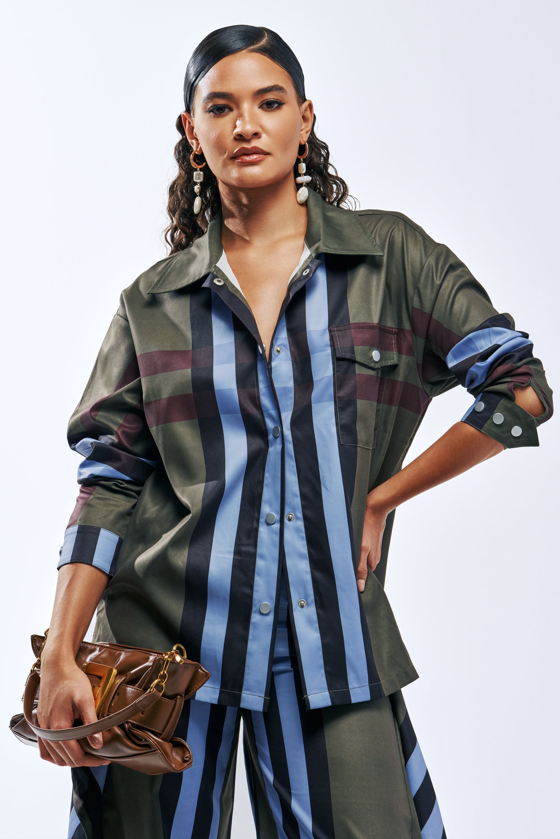 A woman wears a LUXURY LIFE PLAID BUTTON DOWN IN GREEN shirt with matching trousers, holding a brown handbag.