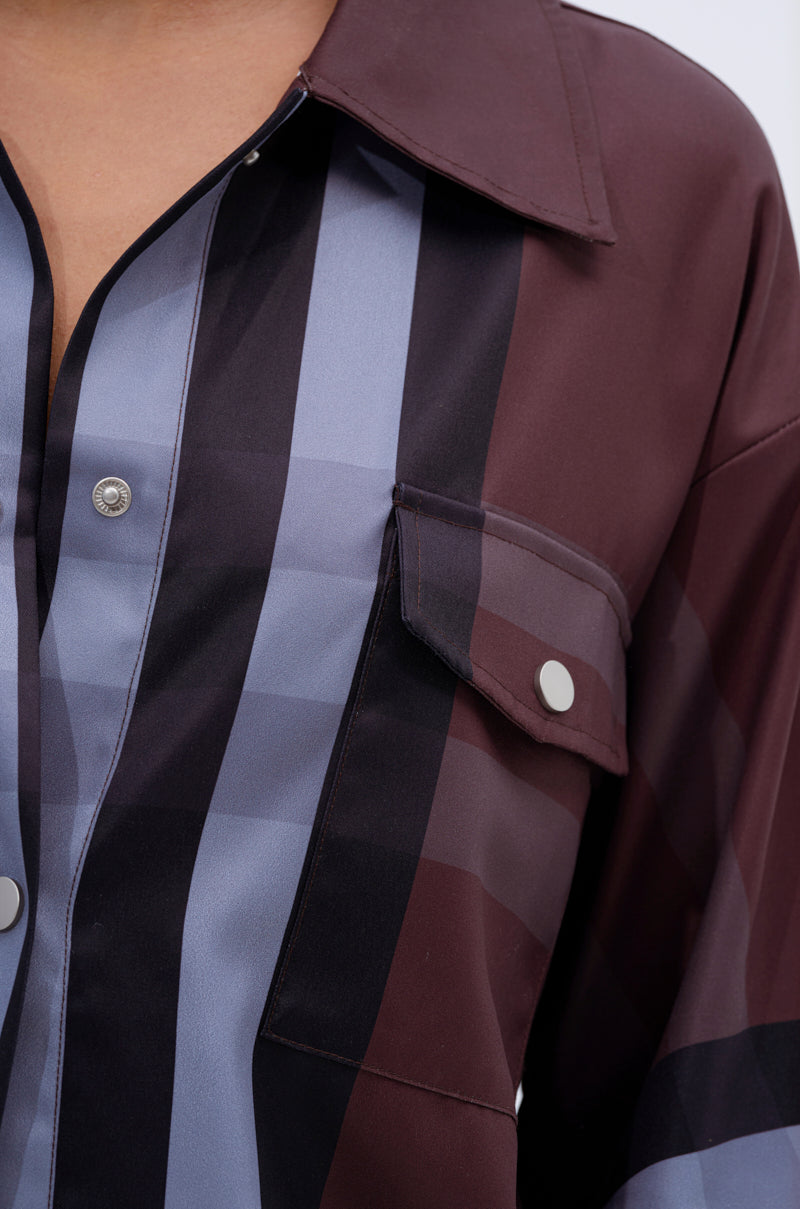 Close-up of a person wearing the LUXURY LIFE PLAID BUTTON DOWN—a plaid shirt in burgundy, black, and blue featuring a collar, chest pocket with flap, and silver snap buttons.