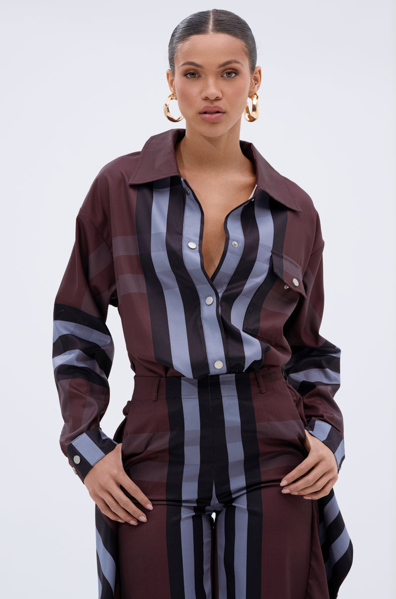 A woman wears the LUXURY LIFE PLAID BUTTON DOWN set with high-waisted pants. Sophisticated brown, black, and gray vertical stripes complement her slicked-back hair, gold hoops, and confident pose against a plain background.