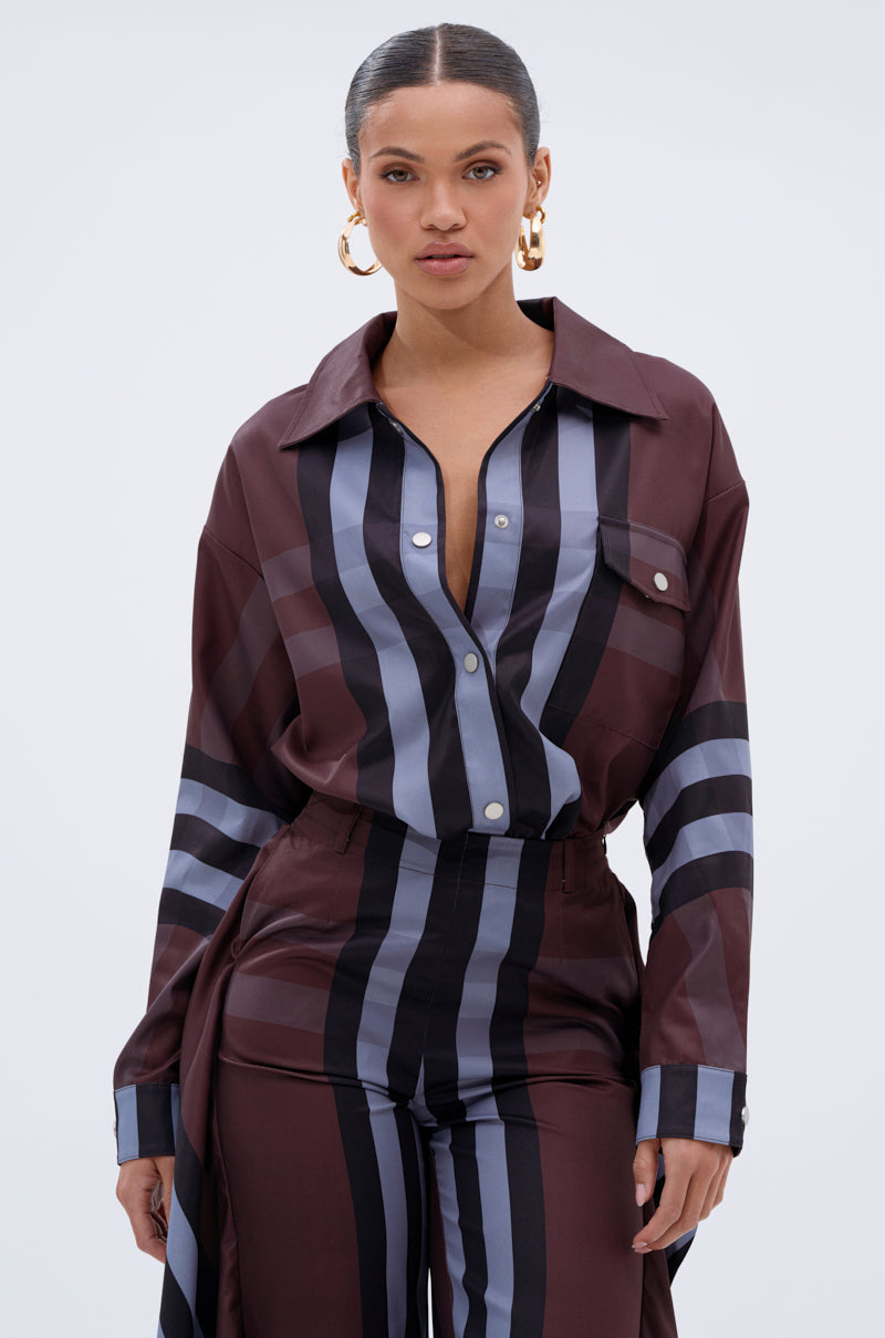 A woman styles the LUXURY LIFE PLAID BUTTON DOWN with high-waisted striped pants and gold hoop earrings, finishing her elegant look with her hair pulled back.